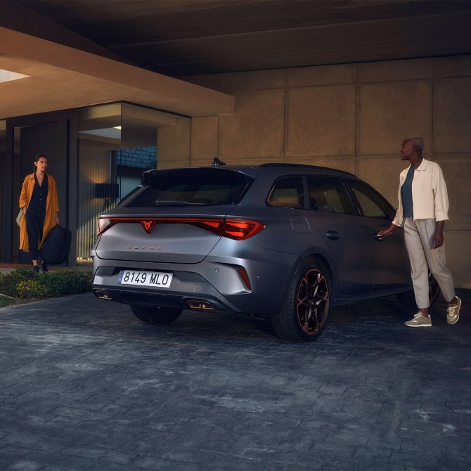 Szara CUPRA Leon Sportstourer zaparkowana przed nowoczesnym budynkiem wieczorem.