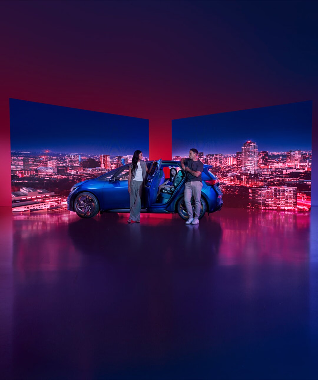 Niebieska CUPRA Born na tle panoramy miasta nocą z parą ludzi obok auta.